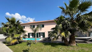 A two-story building with a swimming pool, surrounded by palm trees and a grassy area. - Bed and breakfast with shared pool (10m2) (GODINHAÇOS)