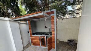 A small outdoor kitchen with a gas stove, wooden cabinets, and a concrete floor.