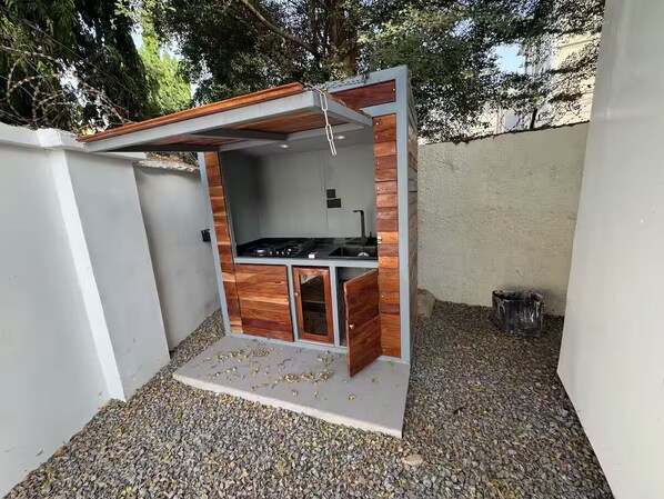 Une petite cuisine extérieure équipée d’une cuisinière à gaz, de meubles en bois et d’un sol en béton.