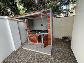 Eine kleine AuĂenkĂŒche mit Gaskocher, HolzschrĂ€nken und einem Betonboden.