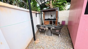 Un patio exterior con mobiliario de mimbre, una parrilla y un muro rosa.