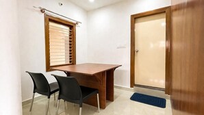 Une pièce avec une table en bois, deux chaises noires, une fenêtre avec des stores, une porte et un tapis bleu.