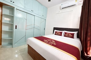 A hotel room with a bed, a wardrobe, and an air conditioning unit.