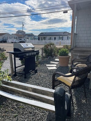 A patio with a grill, wicker furniture, and a view of houses in the background.