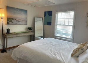 A bedroom with a bed, a desk with a mirror, a lamp, and a window with blinds.