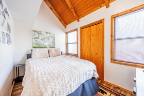 A bedroom with a bed, a nightstand, a wooden door, and a window with blinds. - Cozy Cabin in Black Bear (Davis)