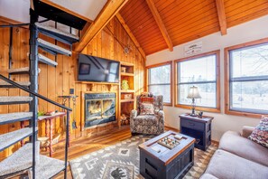 A wooden interior with a fireplace, a television, a patterned armchair, a sofa, and a staircase. - Cozy Cabin in Black Bear (Davis)
