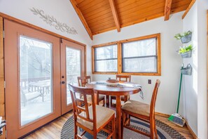 A dining area with a wooden table and chairs, a decorative wall piece, and a window with blinds. - Cozy Cabin in Black Bear (Davis)