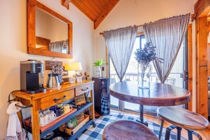 Um quarto acolhedor com um espaço para café em madeira, uma mesa redonda e um detalhe de janela quadriculado.