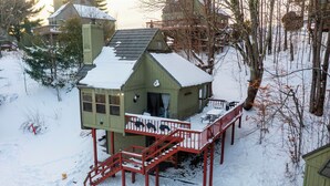 Een besneeuwde houten chalet met balkon, wenteltrap en klein terras.