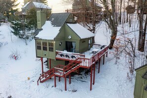 Uma cabana de madeira coberta de neve com varanda, escadaria e um pequeno terraço.