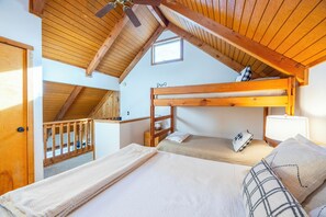 Quarto com duas beliches, vigas de madeira no teto, uma janela pequena e uma porta.