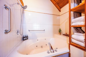 Ein Badezimmer mit einer Badewanne, einer Dusche, einer Handstange und einem Regal mit Handtüchern.