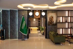 A lobby with a green flag, clocks, a horse painting, and a sofa. - Jawharat Al Nafel Serviced Apartments (Riyadh)