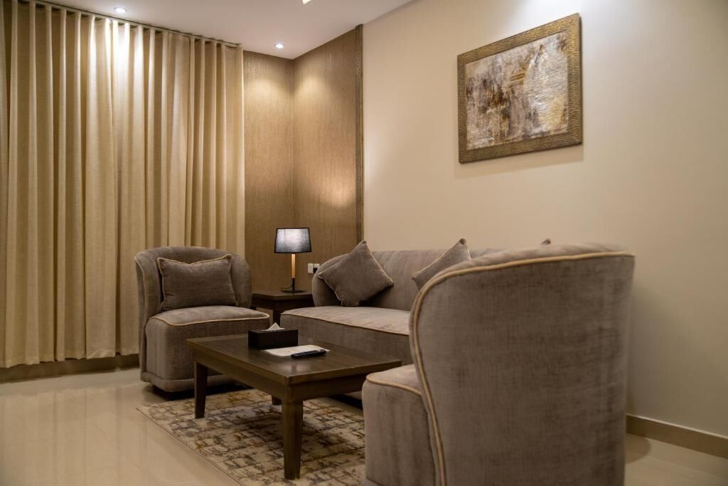 Ein Wohnzimmer mit einer Couch, zwei Sesseln, einem Couchtisch, einer Lampe und einem Gemälde an der Wand.
