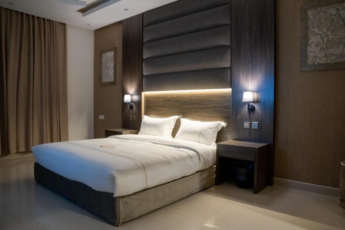 A modern hotel room with a large bed, bedside lamps, a nightstand, and a wall-mounted light fixture.