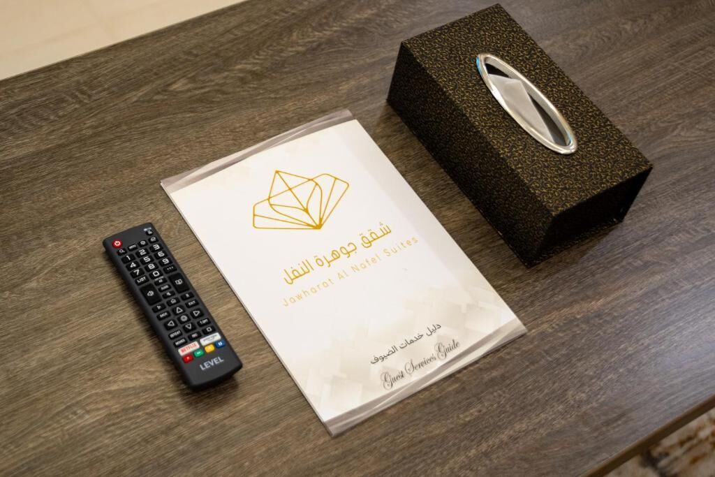 A remote control, a booklet with hotel information, and a textured box on a wooden surface.