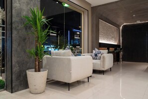 A modern lobby with two sofas, a large potted plant, and a view of the cityscape through large windows. - Jawharat Al Nafel Serviced Apartments (Riyadh)