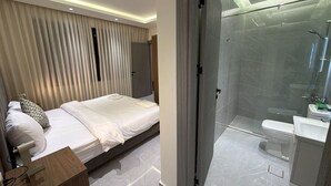 Ett modernt hotellrum med en säng, ett nattduksbord och en duschavdelning med glasväggar.