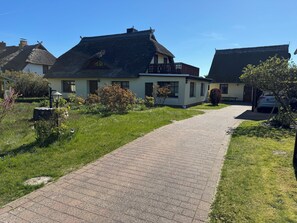Een pad dat leidt naar een huis met een rieten dak, omgeven door groen en een geparkeerde auto.
