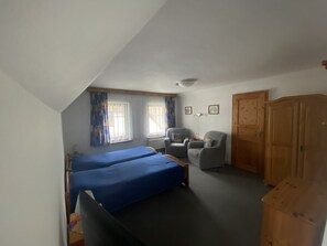 Een kamer met twee bedden, een stoel, een kast en twee ramen met gordijnen.