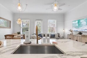 Eine moderne Küche mit Marmorarbeitsplatte, integriertem Spülbecken, Pendelleuchten und Deckenventilator.
