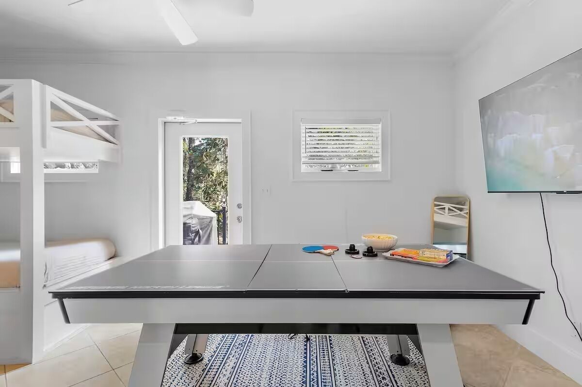 A ping pong table in a room with a white wall, a window, and a door leading outside.