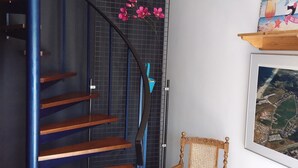 A staircase with wooden steps and a blue railing, a chair with a green cushion, and a framed picture on the wall. - This studio is located 300m from the beach and the sea. (Petten)