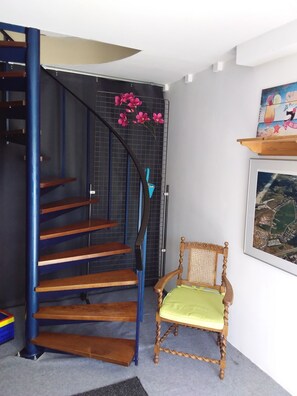 Eine Treppe mit Holzstufen und einem blauen Geländer, ein Stuhl mit einem grünen Sitzkissen und ein gerahmtes Bild an der Wand.
