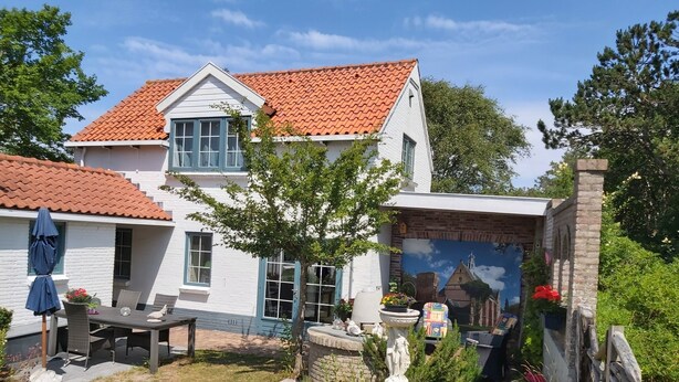 A two-story house with a red-tiled roof, a patio with outdoor furniture, and a mural on the side. - This studio is located 300m from the beach and the sea. (Petten)