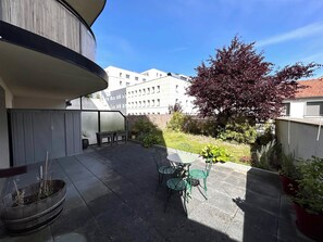 A patio with a table and chairs, a potted plant, and a view of a building in the background. - Le millésime Vesle | Hypercentre | 6 couchages (Reims)
