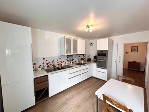 A modern kitchen with white cabinetry, a built-in oven, and a dining area with a wooden table and chair. - Le millésime Vesle | Hypercentre | 6 couchages (Reims)