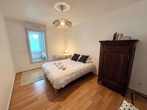 A bedroom with a bed, a wooden wardrobe, a window, and a ceiling light fixture. - Le millésime Vesle | Hypercentre | 6 couchages (Reims)