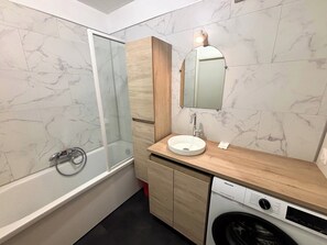 A modern bathroom with a glass-enclosed shower, a sink with a mirror, and a built-in washing machine. - Le millésime Vesle | Hypercentre | 6 couchages (Reims)