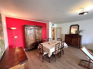 A dining area with a wooden table, chairs, a cabinet, and a red wall. - Le millésime Vesle | Hypercentre | 6 couchages (Reims)