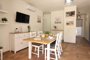 Un comedor con una mesa de madera, sillas blancas, un televisor montado en la pared y obras de arte en las paredes.