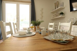 A dining area with a wooden table, white chairs, a buffet setup, and a view through a glass door.
