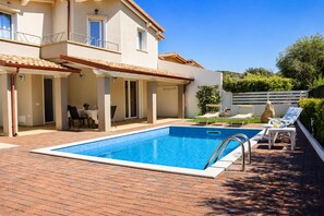 Una piscina con zona de patio, un espacio de estar cubierto y vistas a una colina.