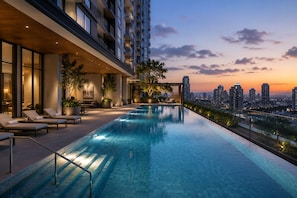 Piscina infinita no terraço com espreguiçadeiras, plantas em vasos e vista para o horizonte da cidade ao pôr do sol.