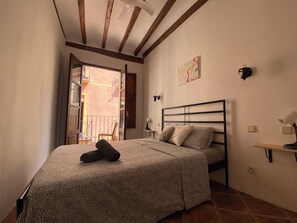 Ein Schlafzimmer mit einem Bett, einem Nachttisch, einer Wandlampe und einem Fenster mit Blick nach draußen.