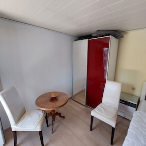 A small room with a bed, two white chairs, a wooden table, and a red wardrobe. - Bungalow in Saxon Switzerland (Sebnitz)