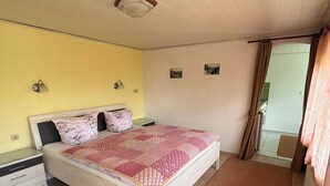 A bedroom with a bed, bedside tables, a window with curtains, and a view of the outside. - Bungalow in Saxon Switzerland (Sebnitz)