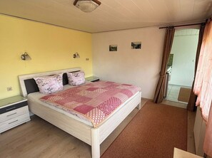 A bedroom with a bed, bedside tables, a window with curtains, and a view of the outside. - Bungalow in Saxon Switzerland (Sebnitz)