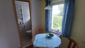 A room with a dining table, chairs, a window with curtains, a radiator, and a door leading to a bathroom. - Bungalow in Saxon Switzerland (Sebnitz)