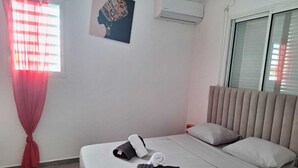 Ein Hotelzimmer mit Bett, Fenster mit Jalousien, einer Klimaanlage und einem Wandbild.