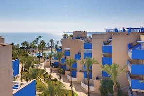 Ein Hotel an der Küste mit mehreren blauen Balkonen, einem Poolbereich und Palmen.