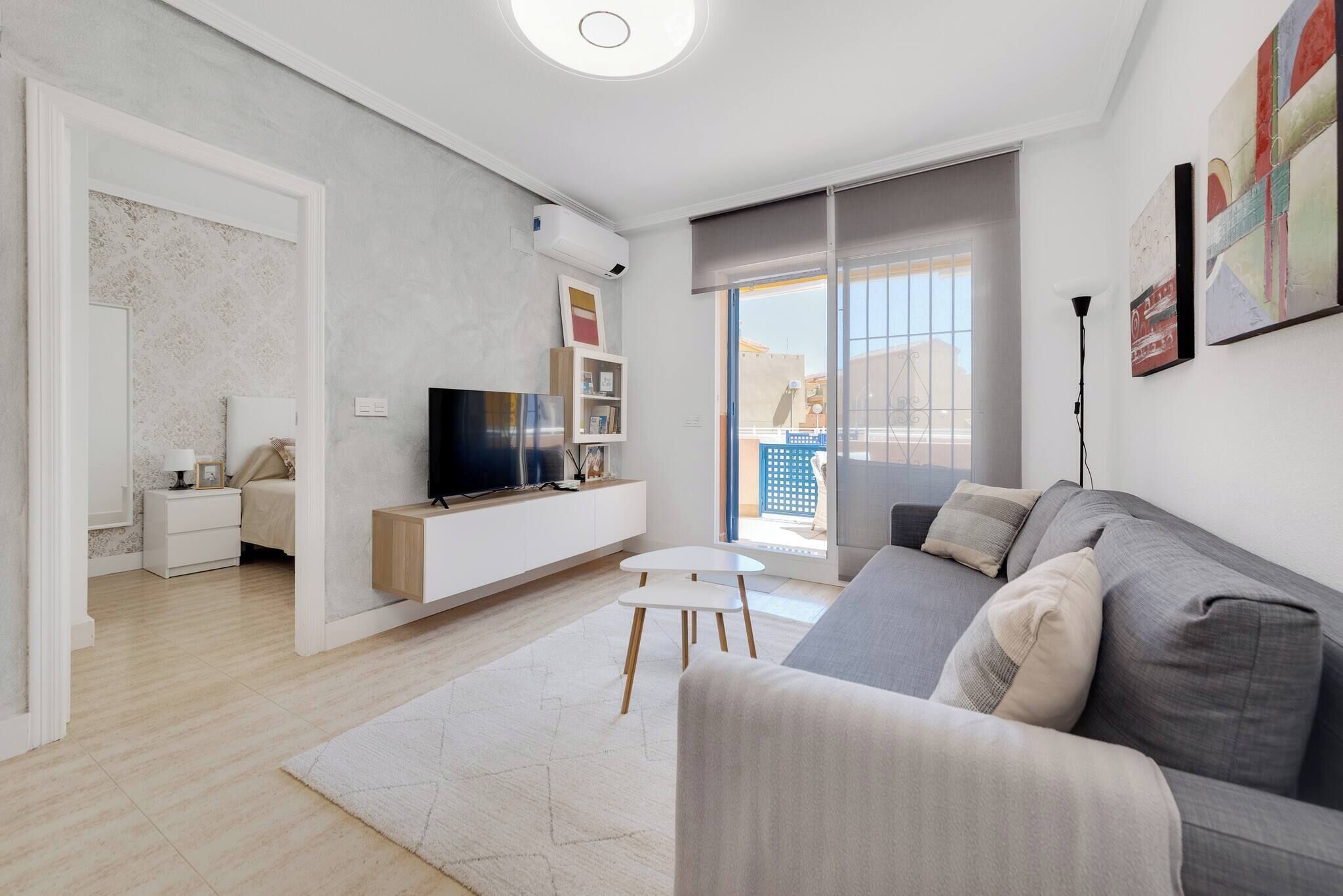 Una sala de estar moderna con un sofá gris, un televisor de pantalla plana, una mesita blanca y una estantería.