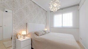Une chambre à coucher comprenant un lit, une table de chevet, un miroir et une fenêtre laissant entrer la lumière naturelle.