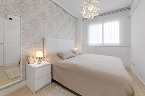 Ein Schlafzimmer mit Bett, Nachttisch, Spiegel und einem Fenster mit Tageslicht.