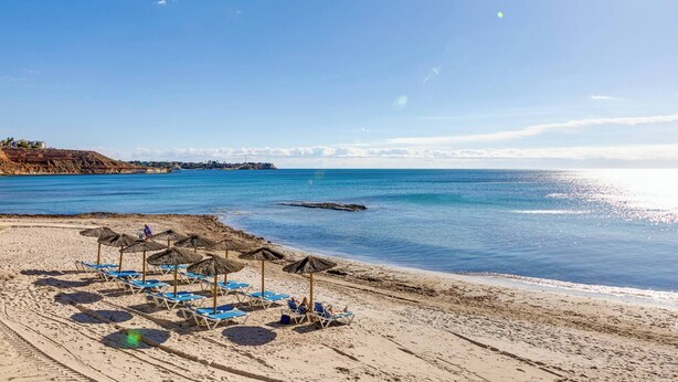 Une plage avec des chaises longues et des parasols, un ciel dégagé et une mer calme.